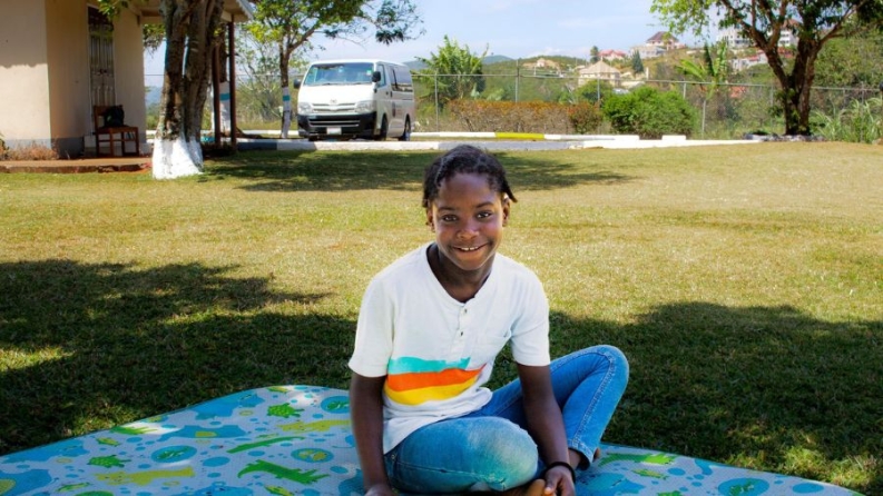 Kimoya sits on a blanket in the center of Gift of Hope's green lawn.