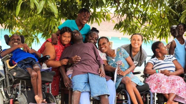 A group of residents sits laughing with staff and volunteers.